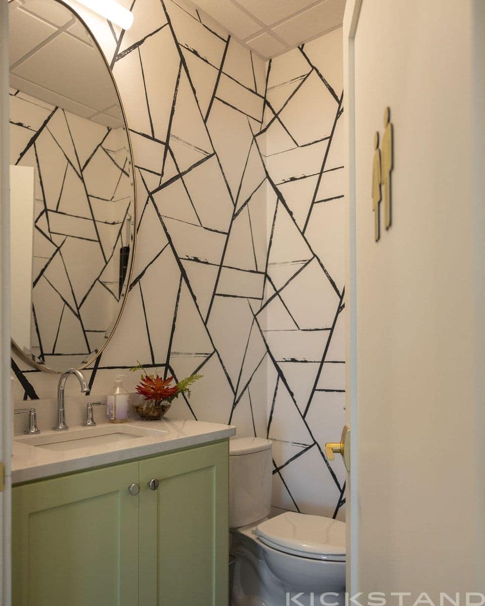 Columbia restroom with a geometric mural, green vanity, and round mirror