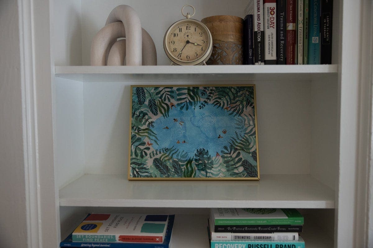 Bookshelf with therapy books and a framed pond print in the Lexington office